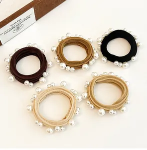 Detailed set of five elastic pearl hair ties in assorted earth-toned colors on a beige base