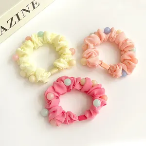 Trois chouchous colorés à perles en jaune, rose et fuchsia sur un fond neutre