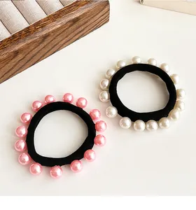 Détail de chouchous à perles roses et blanches avec élastiques épais sur plateau bois