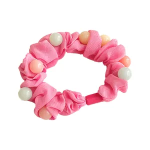 Chouchou rose avec perles pastel et tissu plissé sur un fond blanc propre et net