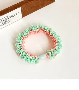 Detail of two-tone pleated scrunchie in mint green and coral pink with a resin bead