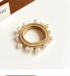 Macro detail of high-elasticity beige hair tie with elegant white faux pearl embellishments