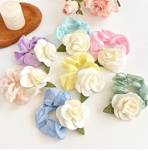 Détail de chouchous en satin colorés avec des fleurs de camélia blanches en six tons pastel