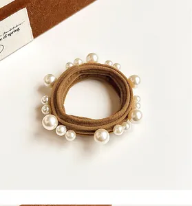 Detail of a brown elastic hair tie with white pearls on a minimalist warm background