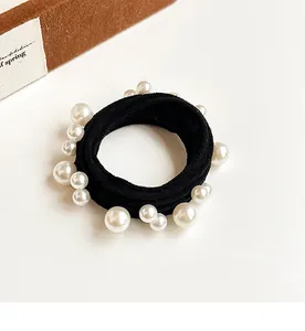 Detail of a high-elastic black hair tie featuring elegant white faux pearls on a desk