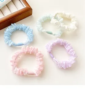Flat lay of five pearlescent organza scrunchies in pastel macaron colors with wood tray
