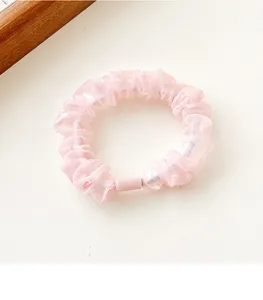 Detail of pink organza scrunchie featuring pleated mesh texture and a plastic fastener