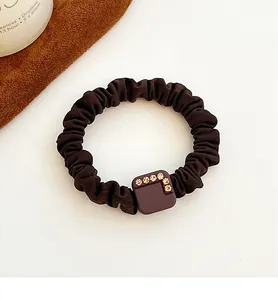 Detail of coffee brown scrunchie with rhinestone square buckle on white background