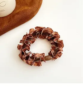 Detailed view of coffee brown ruffled scrunchie with glossy fabric and resin bead detail