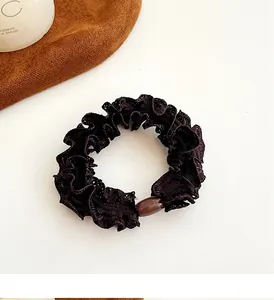 Close-up of a coffee brown ruffled hair scrunchie with a glossy bead and soft fabric texture