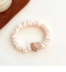 Detailed macro view of a cream fabric scrunchie with a pink rhinestone heart charm