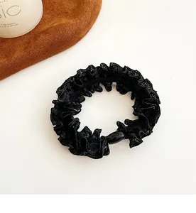 Detail of black lace hair scrunchie with glossy bead ornament on white and brown background