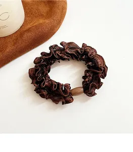 Detail of coffee brown ruffled scrunchie with a decorative oval bead on white background