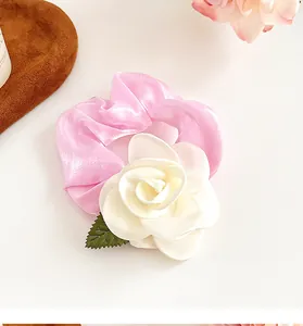 Détail d'un chouchou en satin rose orné d'un camélia blanc et d'une petite feuille verte