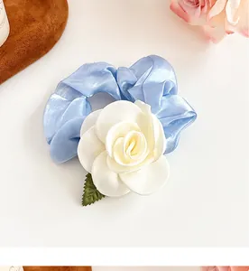Détail d'un chouchou en satin bleu avec fleur de camélia 3D et une petite feuille