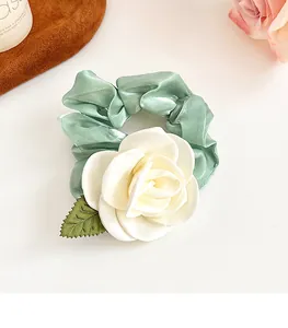 Détail d'un chouchou en satin vert pâle avec une grande fleur de camélia en tissu blanc