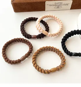 Detail of five thick woven hair ties in neutral earth tones with plastic buckles
