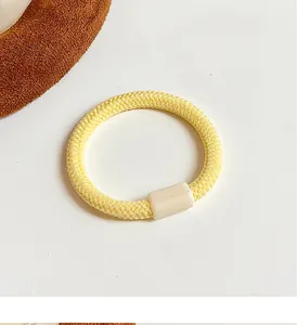 Détail d'un élastique à cheveux tressé jaune vif avec une boucle en plastique beige clair