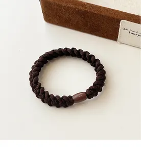 Close-up of a braided dark brown hair tie with a glossy clasp on a soft velvet box