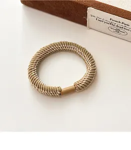 Detail of a thick braided elastic hair tie with gold metallic threads on white surface