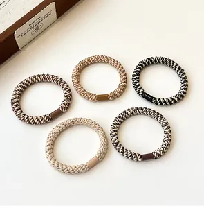 Detailed view of five high-elasticity braided hair ties in neutral tones on flat lay