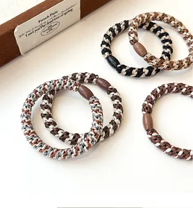 Macro detail of elastic braided hair ties in coffee tones on a warm cream background