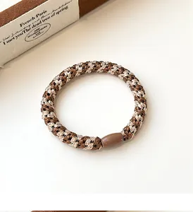 Close-up of woven elastic hair tie with coffee-toned patterns and decorative resin cylinder