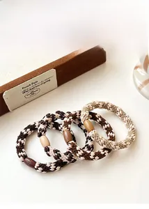 Close-up of four elastic braided hair ties in brown and beige with decorative oval beads