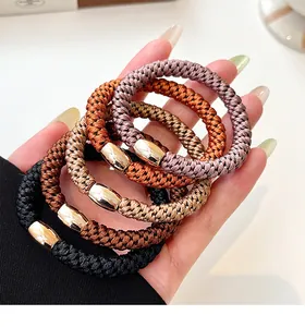 Detail of four elastic braided hair ties in neutral tones with polished gold metal buckles