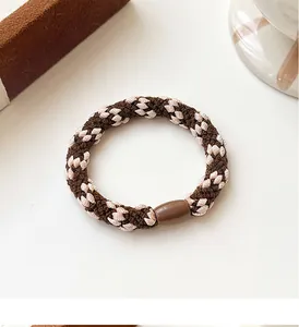 Detail of woven elastic hair tie with brown checkered pattern and resin bead accessory