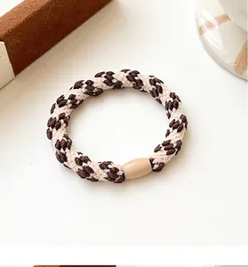 Close-up of woven dual-tone elastic hair tie with a decorative beige cylindrical buckle