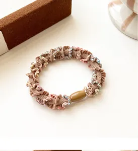 Détail d'un chouchou plissé marron clair avec des perles colorées et une perle en résine