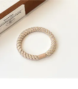 Macro detail of beige woven elastic hair tie with metallic thread and resin buckle