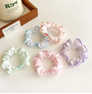 Close-up of five macaron-colored floral hair scrunchies with wavy edges on white desk