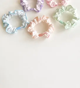 Detail of five pastel scrunchies in blue, purple, pink, orange, and mint green fabric