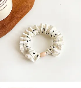 Detailed view of white polka dot hair scrunchie with ruffled edges and resin bead detail