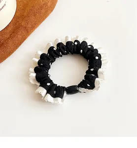 Close-up of black polka dot hair tie with white ruffled edges and elastic band design