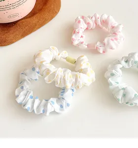 Close-up of four pastel polka dot scrunchies in pink, yellow, blue, and green fabric