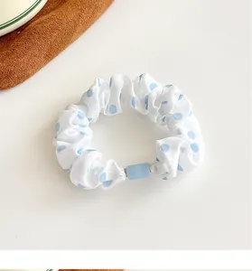 Close-up of white scrunchie with blue polka dots and a blue square fixing piece