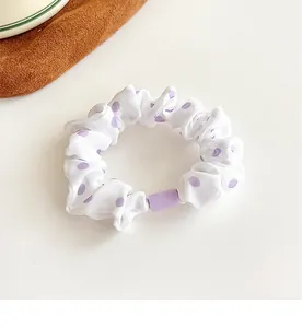 Detail of white fabric polka dot scrunchie with a purple resin buckle on a soft surface