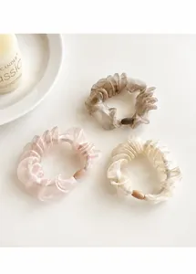 Three organza scrunchies in pink, taupe, and champagne gold next to a candle