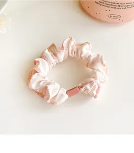Detail view of light pink floral scrunchie with soft fabric texture and plastic accent