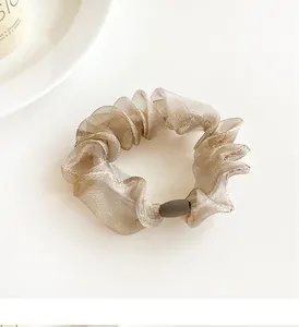 Detail of champagne organza hair scrunchie with grey decorative bead on white desk