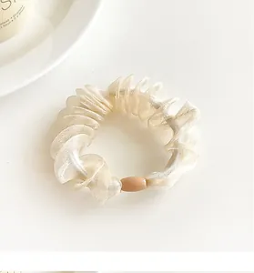 Detail of cream organza scrunchie with pleated texture and decorative oval bead charm
