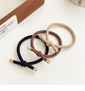 Close-up of three elastic knotted hair ties in black, brown, and beige with gold metal clips