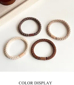 Close-up of four elastic braided hair ties in earth-toned colors on a textured tray