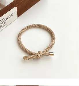 Detail shot of beige knotted hair tie with gold metallic tips on a white surface
