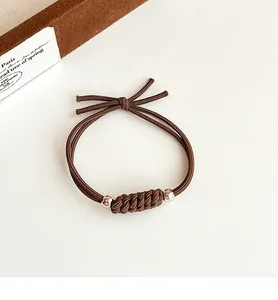 Détail d'un élastique à cheveux tissé marron avec des perles métalliques et un nœud