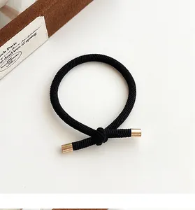 Detail of black woven elastic hair tie with elegant gold metal clasp and knot design
