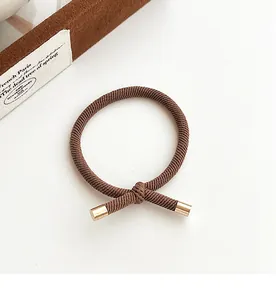 Detail of dark brown braided hair tie with elegant gold metal tips and knotted design